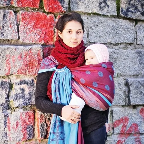 Junge Frau mit ihrem kleinen Baby in einem Tragetuch bei kalten Temperaturen im Winter